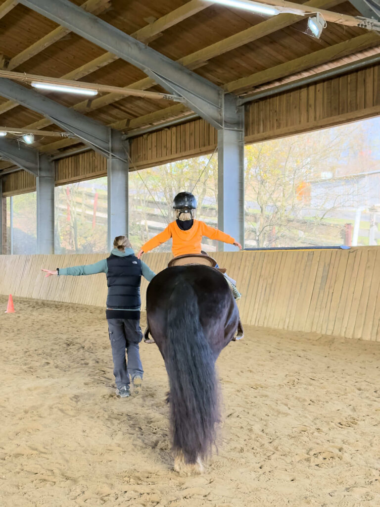 Reiten für Kinder: Ein Kind reitet auf einem Pferd unter Anelitung eines Trainers